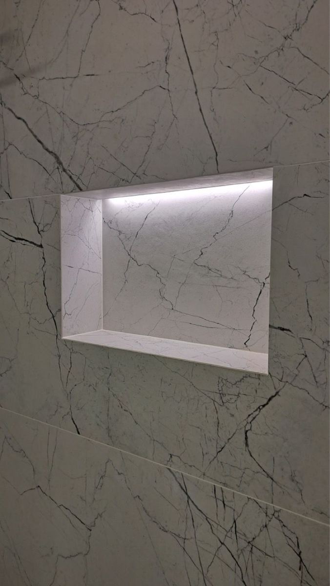 Marble-look large-format shower tile with a lit niche
