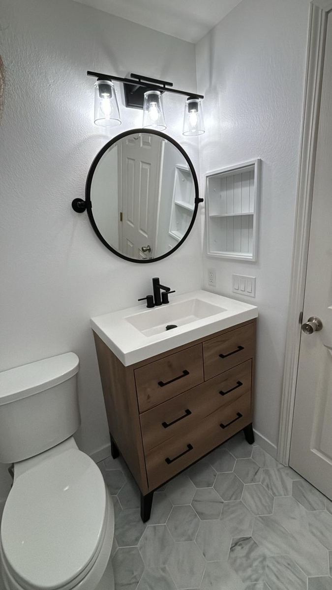 Bathroom with wood vanity, round mirror and marble-look floor tile