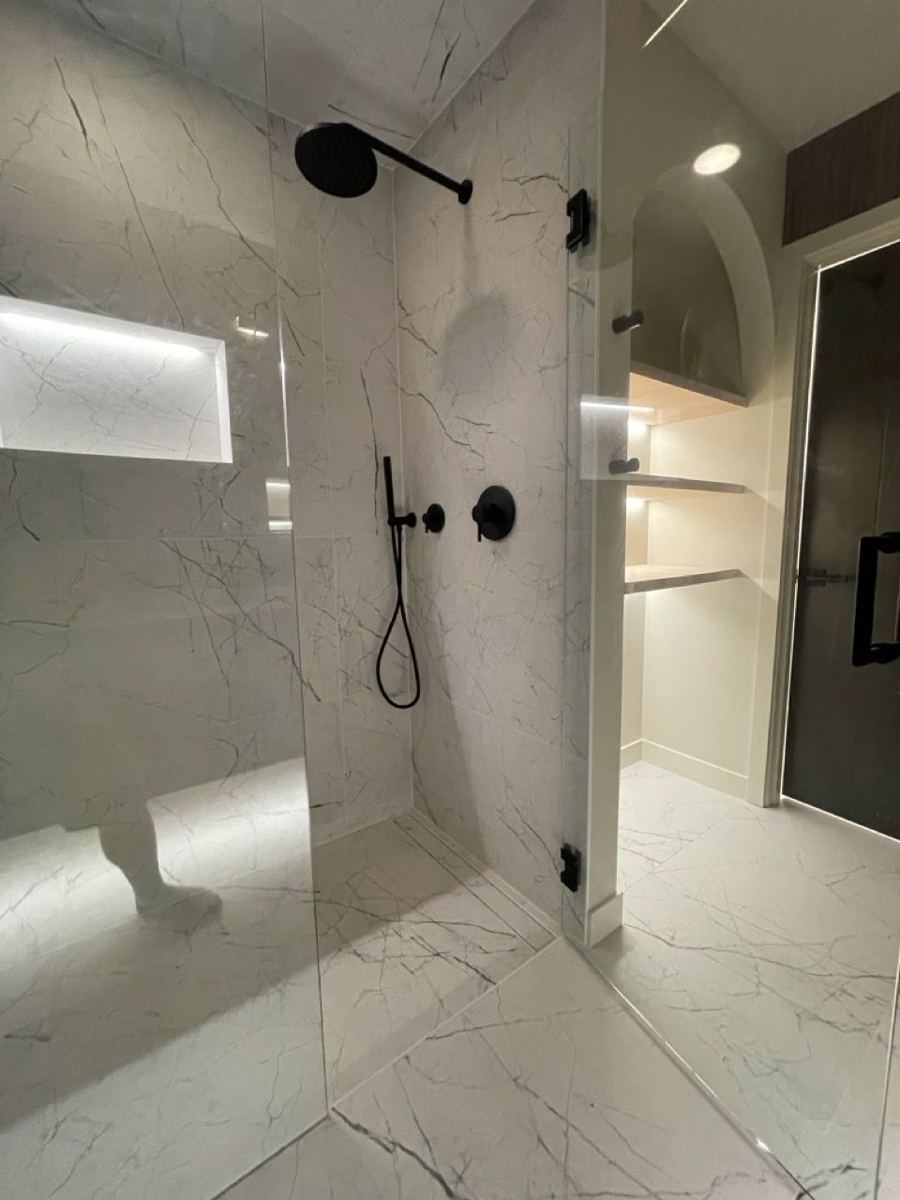 Walk-in shower with large marble-look tile and a lit niche